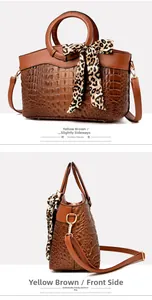 Detail of yellow-brown crocodile embossed handbag with leopard print scarf on handle