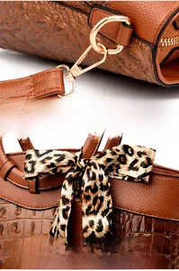 Detail of brown croc-embossed leather tote with gold hardware and leopard ribbon