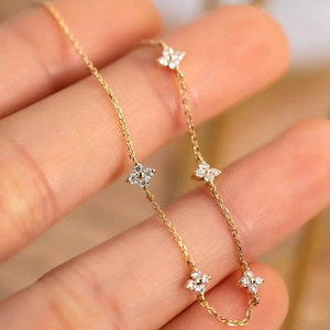 Detail of a gold clover bracelet with five zircon-inlaid flowers on a delicate chain