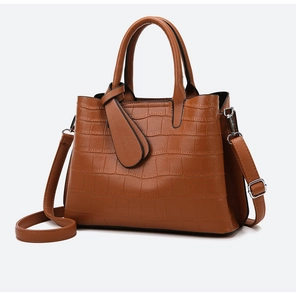 Detail of a brown crocodile embossed handbag with silver metal rings and straps
