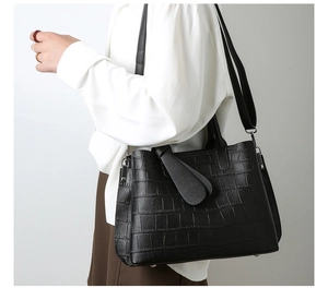 Detail of black crocodile embossed handbag with metal feet and detachable strap
