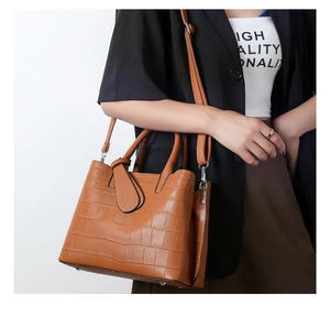 Detailed view of brown crocodile-embossed tote bag with shoulder strap and metal feet