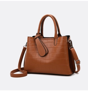 Detail of brown crocodile embossed leather tote bag with sturdy handles and shoulder strap