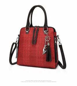 Detail view of red plaid tote bag with cat charm, tassel detail and brown rolled handles