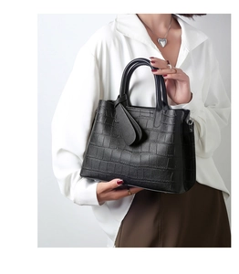 Detail of black crocodile embossed handbag with silver hardware held by a model