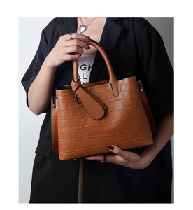 Detail of brown crocodile embossed leather handbag with elegant knot strap and top handle