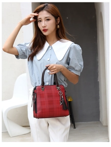 Outdoor lifestyle shot of a red plaid handbag with leather handles and tassel detail