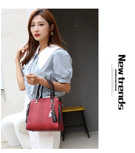 Deep red checkered handbag with cat pendant and tassel held by a fashion model