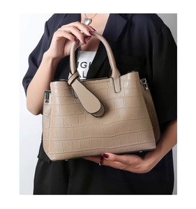 Close-up of khaki crocodile-patterned tote bag held by a model in a black blazer