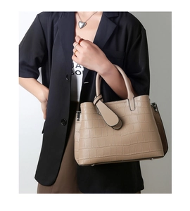 Detail of beige crocodile embossed tote bag held by model wearing a black blazer