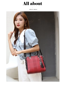 Red plaid handbag with leather tassel and cat charm shown on model in urban setting