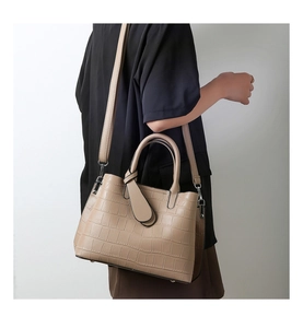 Detail of khaki crocodile embossed shoulder bag with dual handles and metal hardware