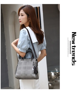 Close-up of gray plaid handbag with brown handles and a cute silver cat charm