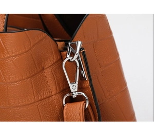 Close-up of shiny silver metal lobster clasp and embossed crocodile texture on brown bag