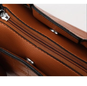 Detail of caramel brown textured leather handbag featuring silver zipper and magnetic closure
