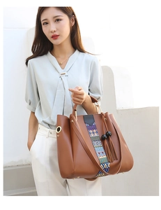 Détail du sac en cuir marron avec sangle tissée colorée, pompons et poignée en métal