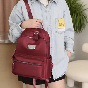 Women's burgundy oxford cloth backpack with multiple zipper pockets and metal plate detail