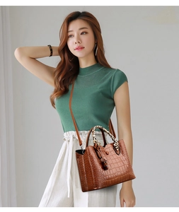 Brown crocodile texture handbag with leopard print handle worn by a model in a green sweater