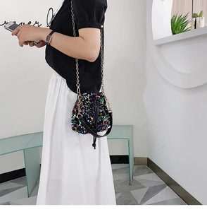 Detail of colorful sequins bucket bag with gold chain strap worn by a model in interior