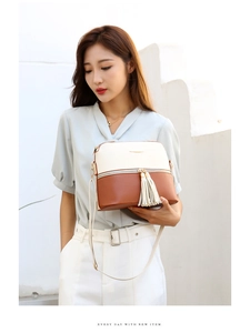 Detail of contrast stitch shoulder bag with tassel and metal zipper against white wall