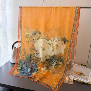 Detail of orange floral silk scarf featuring white peony prints and geometric borders