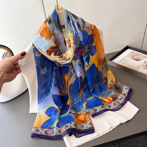 Eleganter langer Seidenschal mit blauen Lilien und Pfauenfedern über weißem Stricktop