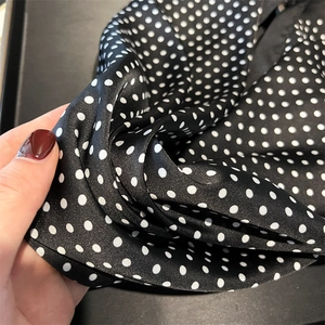 Detailed view of black silk scarf with white polka dots showing soft fabric folds