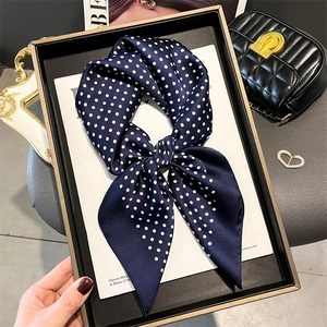 Navy blue polka dot silk scarf tied in a bow on a gift box for a luxury aesthetic