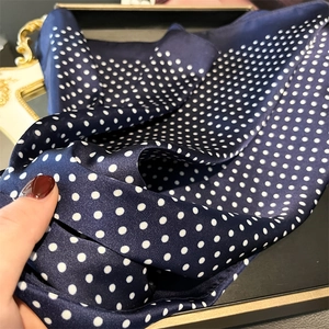Detailed close-up of dark blue silk-like scarf with white polka dots and satin sheen