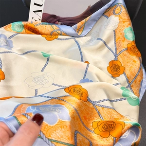 Detail of silk-like square scarf with elegant orange floral prints and blue rope patterns