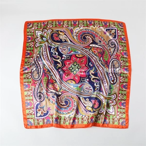 Detailed flat lay of a satin square scarf with paisley floral patterns and orange border