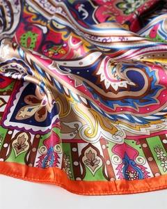 Detailed view of vibrant paisley print silk satin scarf with bright orange hem and glossy texture