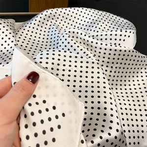 Close-up of premium white silk scarf with black polka dots showing smooth fabric texture