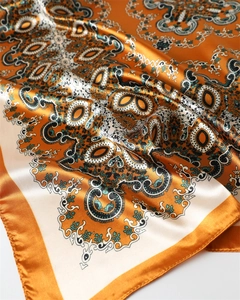 Gros plan du foulard en satin orange et crème avec motif paisley et drapé soyeux