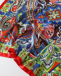 Close-up of vibrant paisley print silk scarf with luxury red satin border and smooth texture
