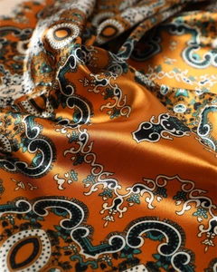 Vue détaillée du tissu satiné orange à motif paisley avec texture soyeuse et reflets