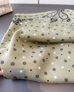 Close-up of sage green paisley square scarf with herringbone texture and star prints