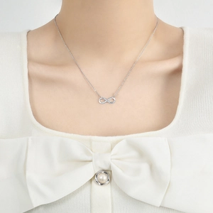 Detail view of a silver infinity pendant necklace with pavé zircons on a female neck