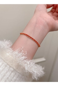 Detailaufnahme eines roten geflochtenen Armbands mit Goldperlen auf weißem Pullover