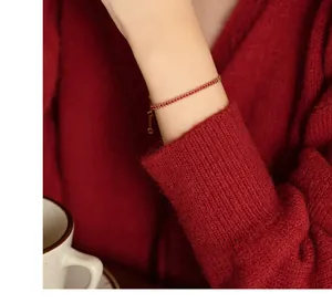 Detail eines eleganten 18K Goldarmbands mit kleinen roten Zirkonsteinen am Handgelenk