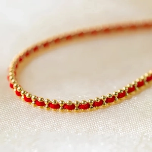 Makroaufnahme eines roten Seilarmbands mit gewebten 18K Goldperlen auf weißer Seide