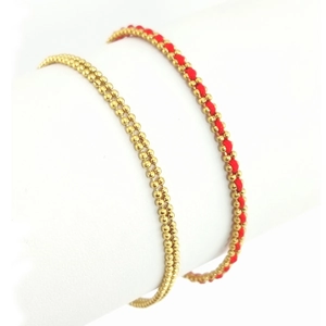 Nahaufnahme von zweilagigen goldenen Perlenarmbändern und geflochtenem Glücksseil