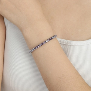 Détail d'un bracelet de tennis argenté serti de zircons violets porté au poignet d'une femme