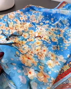 Close-up of translucent blue silk scarf featuring floral prints and traditional patterns