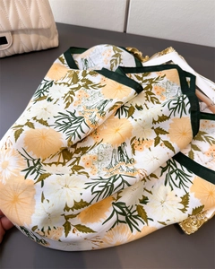 Detail of floral silk scarf with yellow dahlia prints and green borders on elegant tray
