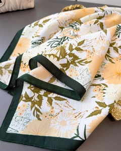 Detail of floral silk scarf showing daisy patterns and dark green rolled edge craftsmanship