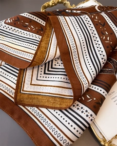 Close-up of caramel brown silk-feel scarf with geometric patterns on a vintage gold tray