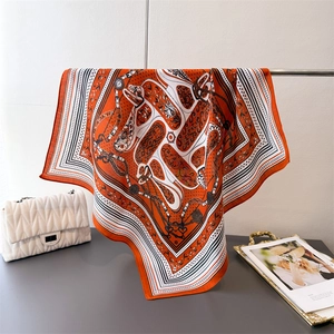 Detailed close-up of silk-textured orange scarf with classic horse harness and chain patterns