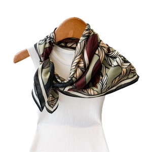 Leaf print silk scarf in olive and burgundy draped on a white ribbed top and wood hanger