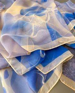 Close-up of blue and white silk scarf with abstract patterns and yellow stitched edges